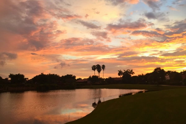 Orange and pink clouds during sunset over residential local homes and neighborhood lake in West Palm Beach county Florida
